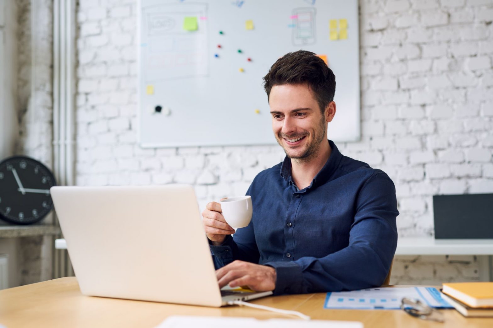 A businessman holding a small mug and working on his laptop in the office.