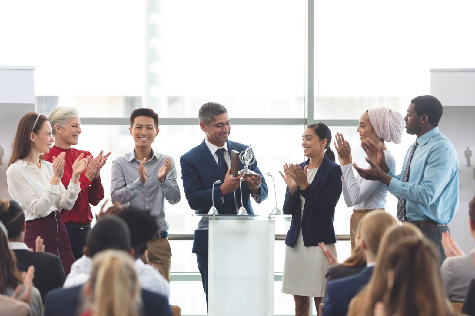 Male in a suit is presenting an award to other professionals who are smartly dressed and clapping.