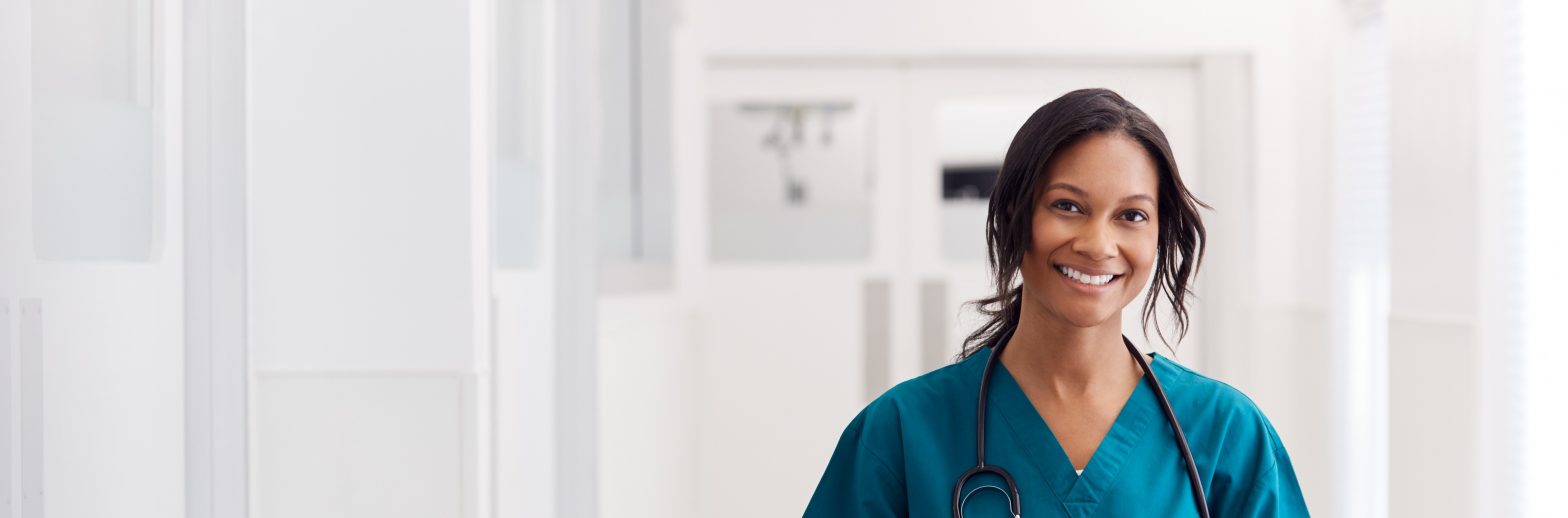 Portrait Of Smiling Female Doctor Wearing Scrubs In Hospital Corridor Holding Digital Tablet