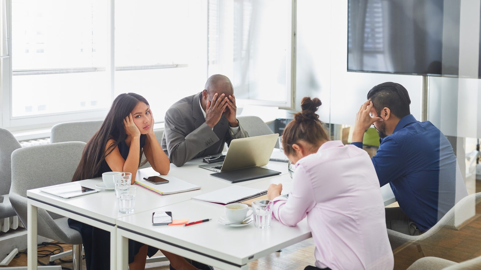 Unhappy staff are sitting around a conference table with their heads in their hands clearly frustrated.