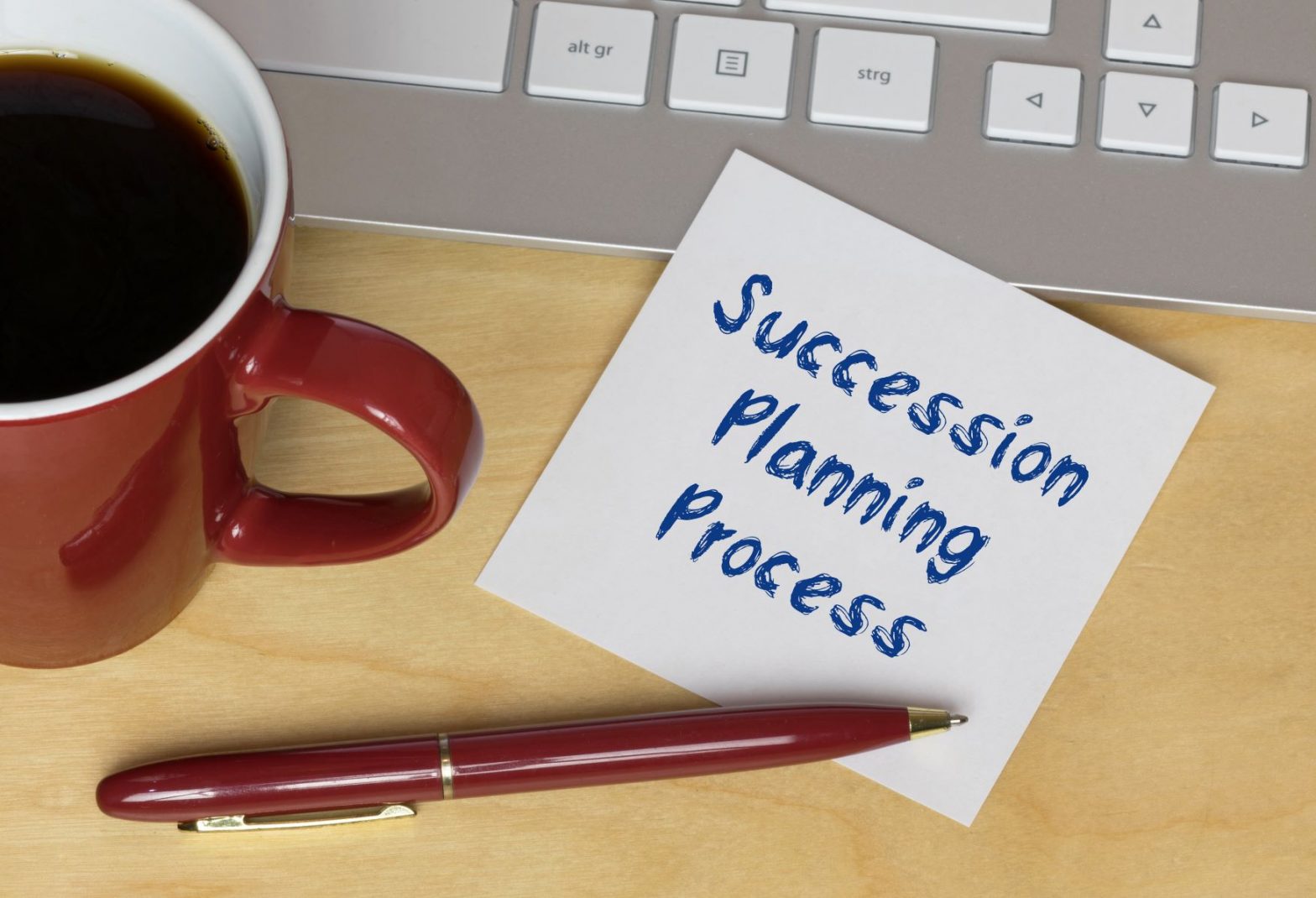 Succession planning process written on a piece of paper place on a laptop next to a mug of coffee.