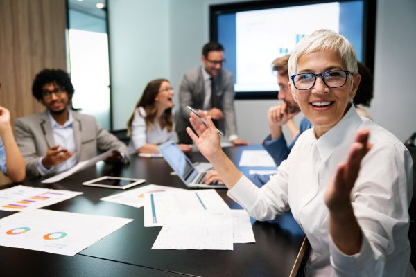 Smiling business person in a mentorship workshop with colleagues behind her laughing and having discussions.