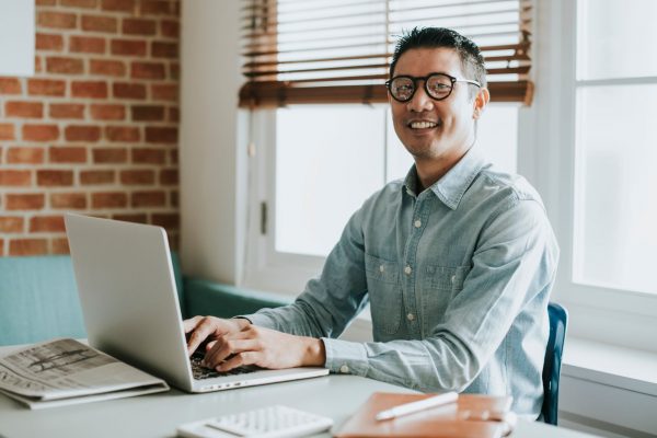 A man wearing glasses and a shirt is working on his laptop.