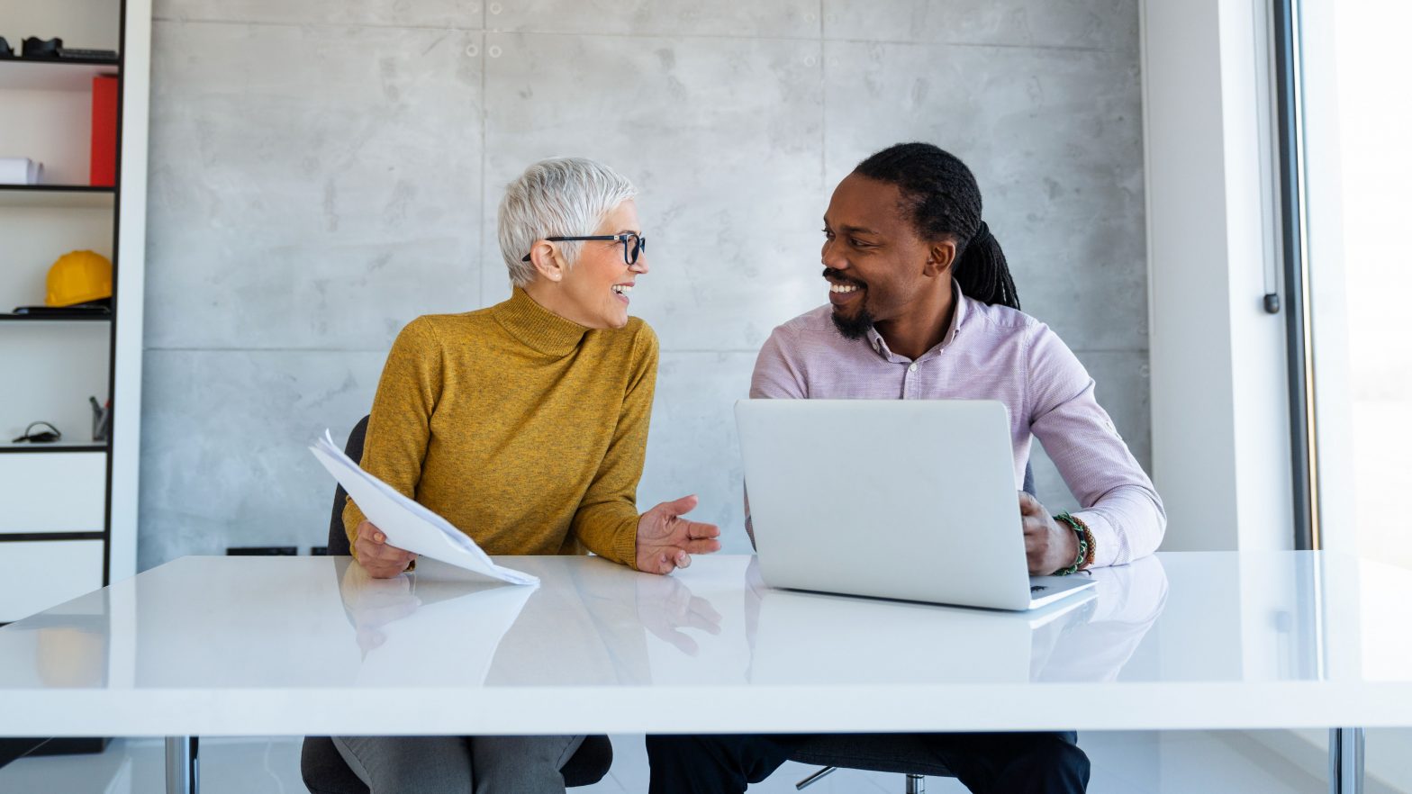 Male and female mentor and mentee in discussion with a laptop and paperwork in front of them