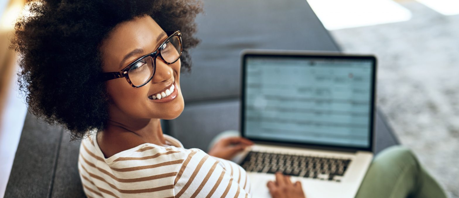 Female wearing glasses smiling at the camera and working on a laptop