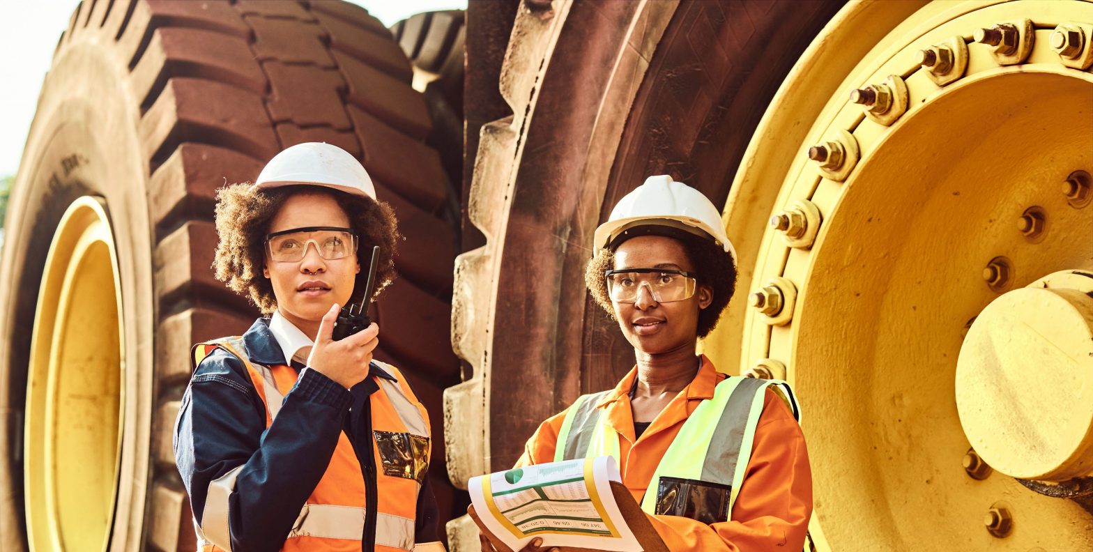 Two female workers in safety jackets standing but giant wheels