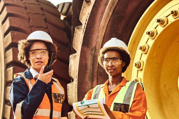 Two female workers in safety jackets standing but giant wheels