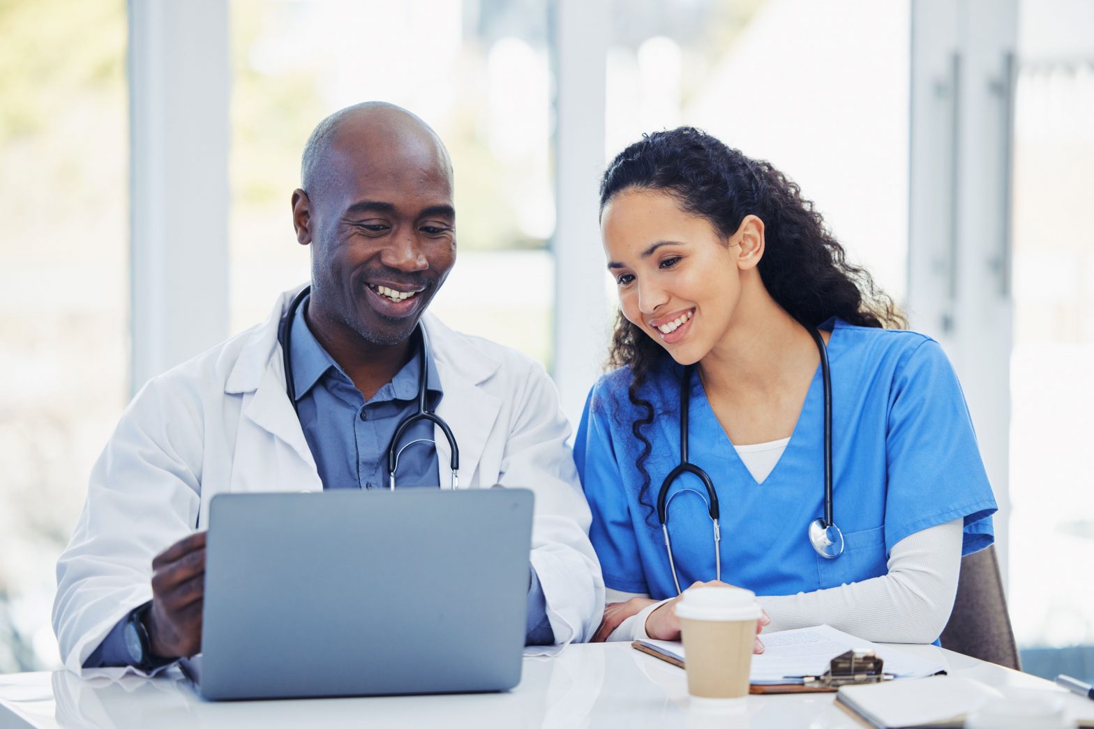 A more experienced medical profession is mentoring a young female. They are both looking at a laptop.