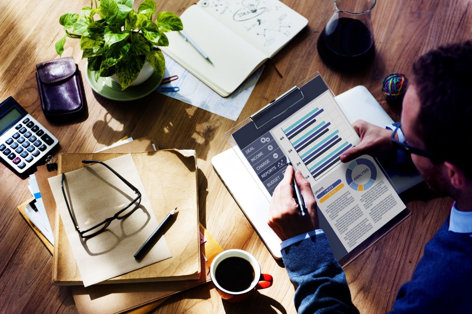 A photograph looking over the shoulder of a businessman looking at stats and information on a clipboard.