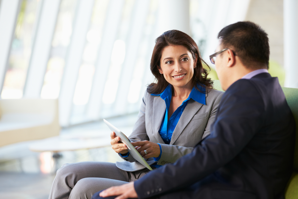 A female mentor is showing her male mentee something on her tablet computer