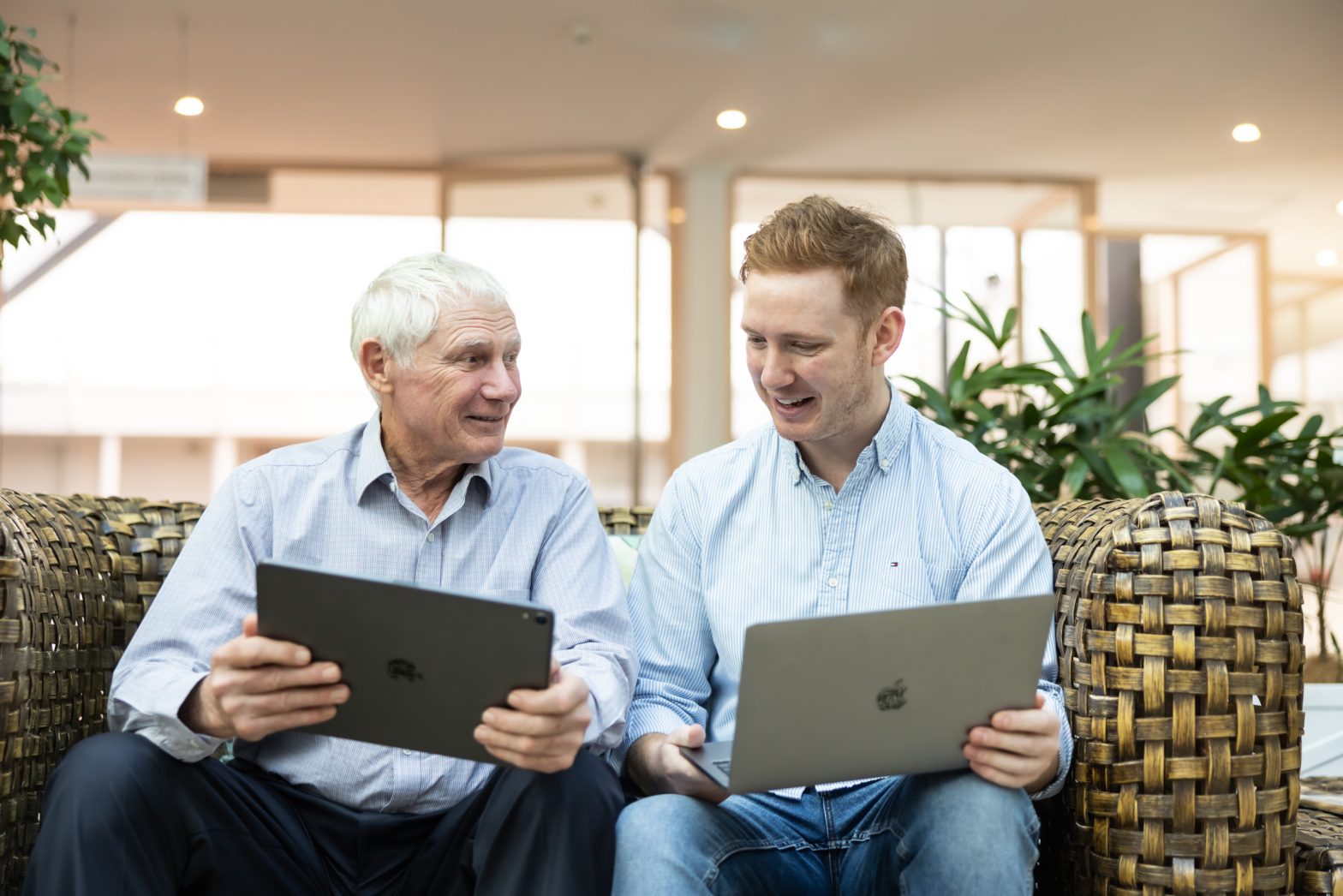 A young man and a senior man in a mentor, mentee relationship looking at devices together.