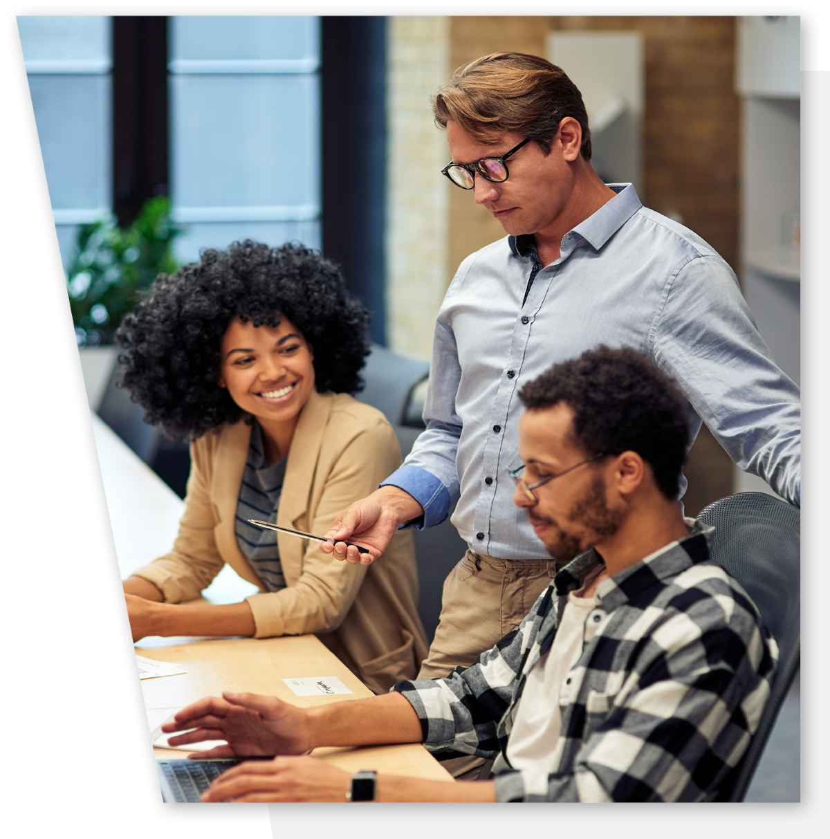 Male wearing glasses mentors and male and female employee who are smiling and listening to instruction.