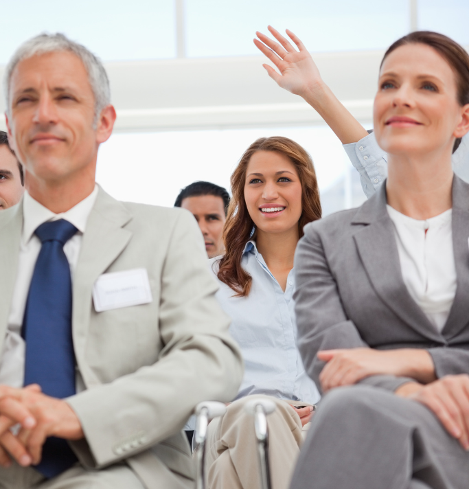 Business people in a training session raise their hands to ask questions.