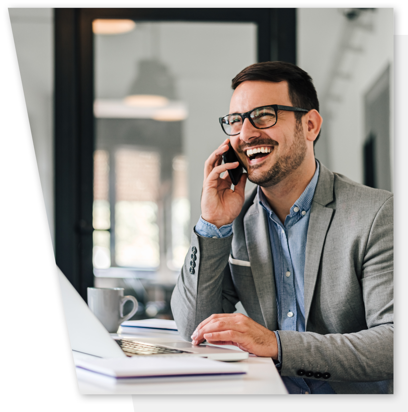 A man wearing glasses and a suit is smiling while on the phone.