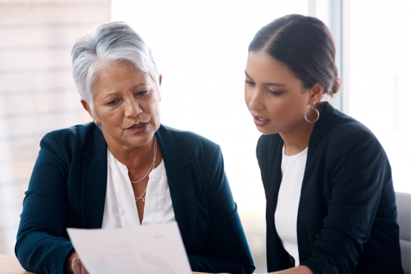 A mentor and mentee are smartly dressed and looking at a paper together.